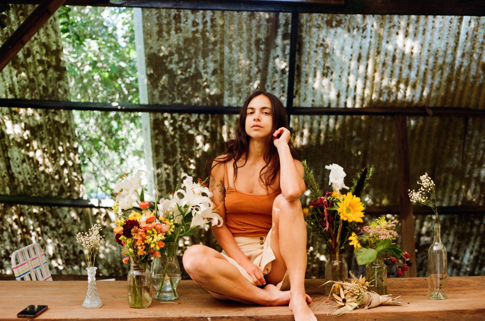 katie sitting cross-legged on a wooden table between jars of wildflowers, lilies and sunflowers