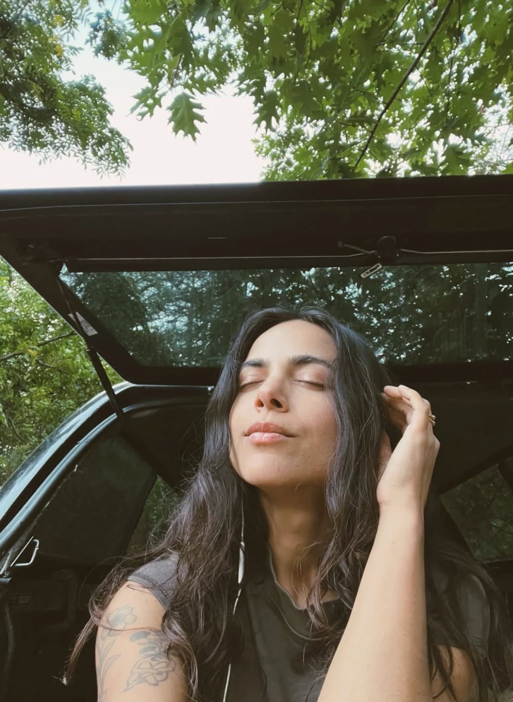 katie with eyes closed under oak leaves, sitting in an open car